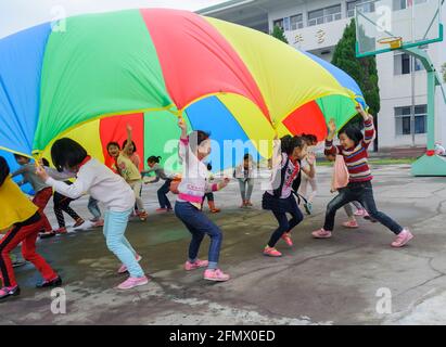 Students from Weiqiao Central Primary School in Xiuning, Anhui, China play with a parachute for the first time. Stock Photo