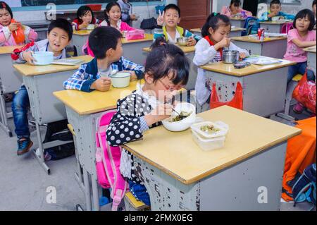 Students from Weiqiao Central Primary School in Xiuning, Anhui, China eating lunch in their classroom. Stock Photo
