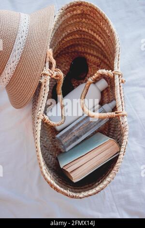 Vertical image of a summer bag with sun cream, a book and sunglasses on it. Perfect set to enjoy a sunny day at the beach. Summer Concept 2021. Stock Photo