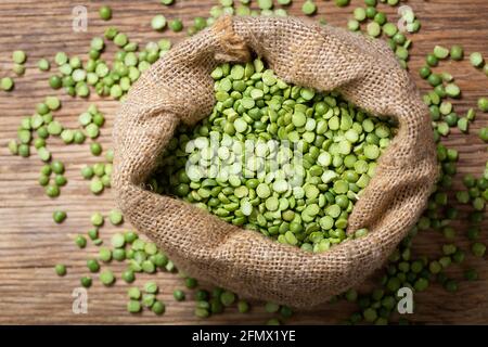 Split dried peas in a sack on a wooden background, top view Stock Photo