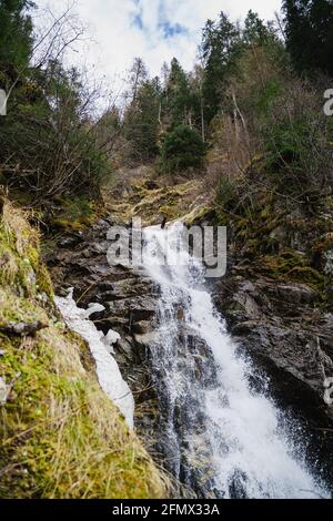Waterfall and brook flowing through boulders in the Austrian Alps, St.Anton. River is surrounded by conifers/trees. Rocks look grey and mossy. Stock Photo