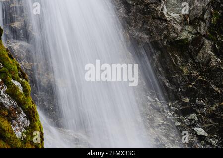 Waterfall and brook flowing through boulders in the Austrian Alps, St.Anton. River is surrounded by conifers/trees. Rocks look grey and mossy. Stock Photo