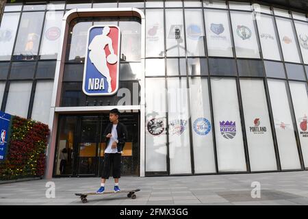 Beijing, China. 10th May, 2021. A kid on a skate board rides past the NBA logo and store on Wangfujing Street in Beijing. Credit: SOPA Images Limited/Alamy Live News Stock Photo