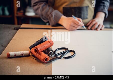 The first stage in the production of shoes is to make an exact pattern from paper, a young shoemaker in uniform at work. Stock Photo