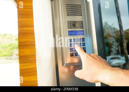 Close up of man hand entering security system code, pressing button with index finger on modern intercom device with blue lcd screen near entrence doo Stock Photo