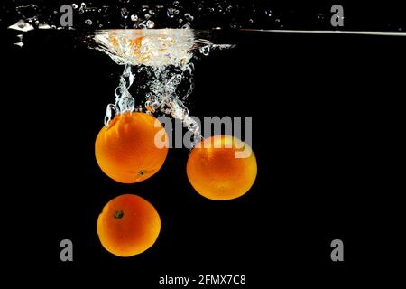 three juicy tangerines in water on a black background Stock Photo