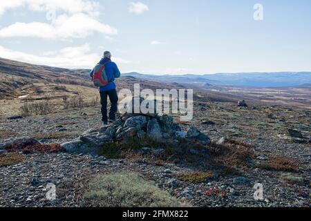 In late autumn, a hiker stands next to a pile of stones that marks Pilegrimsleden and looks down into the valley with the Fokstumyra Nature Reserve Stock Photo