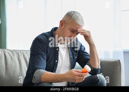 Senior man having headache, holding jar with pills Stock Photo