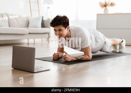 Sporty asian man doing plank watching tutorial on laptop Stock Photo