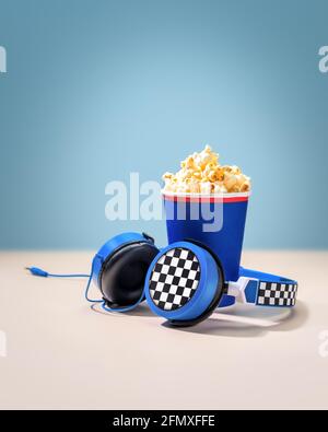 Composition with disposable cup with popcorn and headphones on a pink-blue background with copy space. The concept of watching a movie at home with po Stock Photo