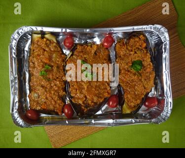 Stuffed Eggplants, Aubergines with Bolognese sauce and Fresh cherry tomatoes in a aluminium platter on a green tablecloth. Top view Stock Photo