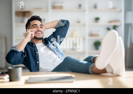 Relaxed arab man freelancer having short break, talking on phone Stock Photo