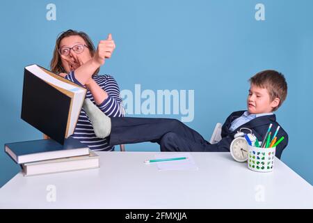 Angry schoolboy boy in uniform with textbooks fights with mom, blue background Stock Photo