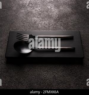 black matte fork with spoon close-up. on a dark background, modern tableware, square photo. Stock Photo