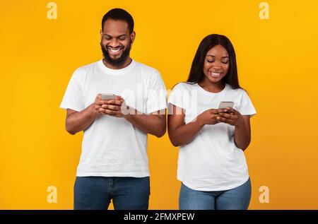 Black couple using smartphones, standing at studio Stock Photo