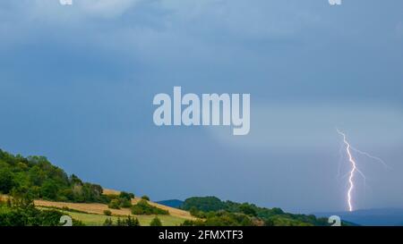 Thunderstorm with lightning over the hilly landscape Stock Photo
