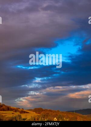 The afternoon sun creates a beautiful three-color scene on the clouds in the sky above the hilly landscape. Stock Photo