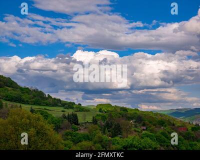 Massive clouds - Cumulonimbus - forming in the blue sky over hilly landscape Stock Photo