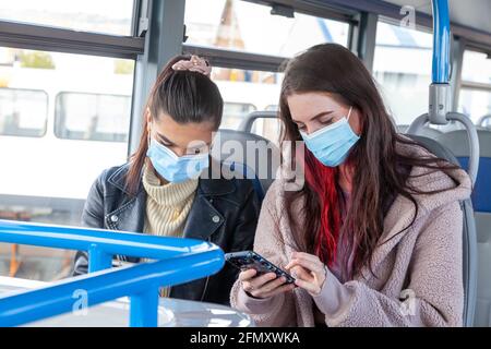Two young women sitting on a bus using their phones Stock Photo