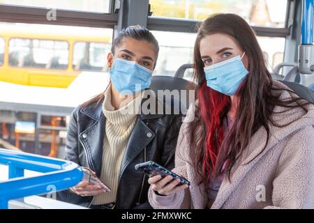 two women on a bus wearing face masks and looking to camera Stock Photo