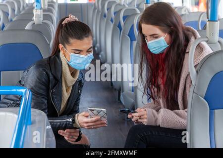 Two female friends on a bus looking at each others phones Stock Photo