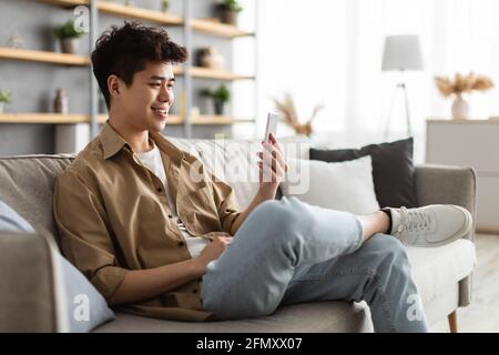 Closeup of smiling asian man using smartphone at home Stock Photo