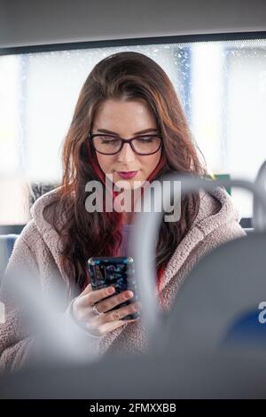 Portrait of young woman travelling by bus looking at cell phone Stock Photo
