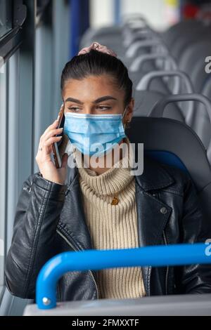 Woman travelling on a bus wearing a face mask and talking on a mobile phone. Stock Photo