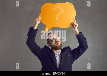 Sceptical businessman in suit and glasses holding speech bubble with question mark Stock Photo