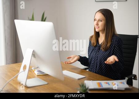 Video conference concept. Young positive businesswoman using computer for video communication with coworkers, colleagues on the distance, female employee holding video meeting Stock Photo