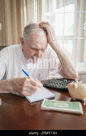 old man in a depression is counting pennies from the pension fund. A worried elderly man saves money in a piggy bank. The pensioner calculates the bud Stock Photo