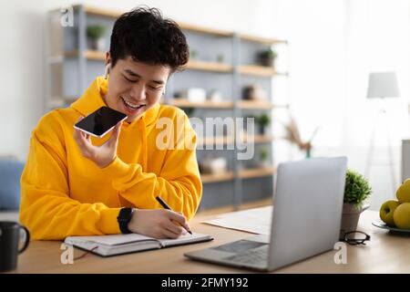 Asian guy using voice assistant on cellphone Stock Photo