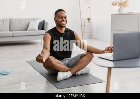 African Man Doing Yoga Online Meditating Sitting At Laptop Indoor Stock Photo