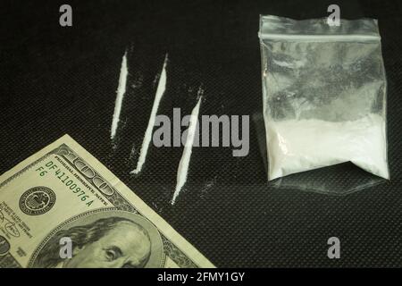 Drugs and dollars on glass, black table. Narcotic powder divided into stripes on a mirrored table, one hundred dollar tube for drug use Stock Photo