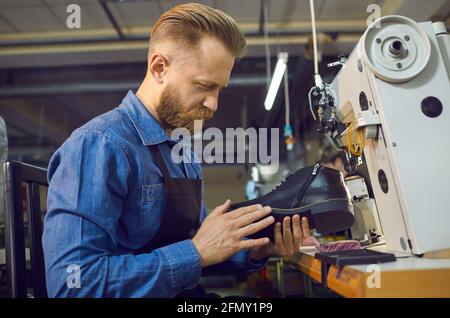 Worker sitting at table with shoe sewing machine and checking quality of footwear Stock Photo