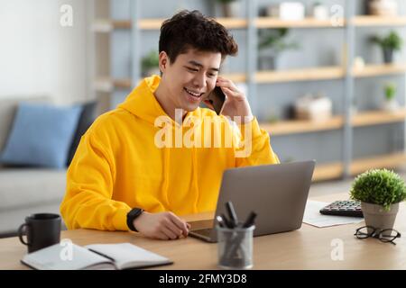 Smiling asian man working and talking on phone at home Stock Photo