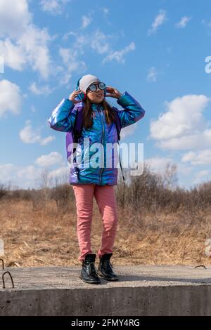 Teenage girl in mirrored sunglasses looks into the sky. Wellness concept. Child listens to music and sings Stock Photo