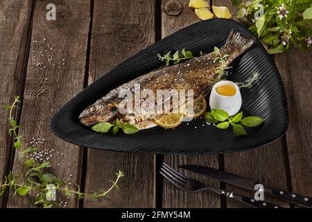 Grilled rainbow trout with lemon and herbs on wooden table Stock Photo