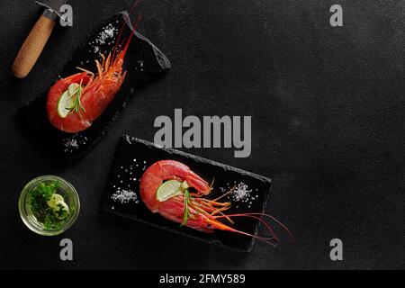 Cooked prawns with condiments and shrimp knife on black background Stock Photo