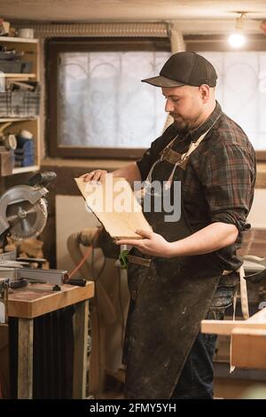 A carpenter holds piece of wood in his hands in workshop Stock Photo