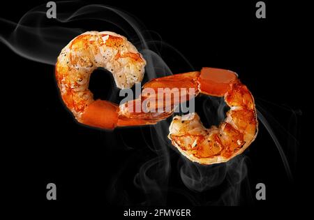 Two grilled shrimp tails in shape of infinity sign on black Stock Photo