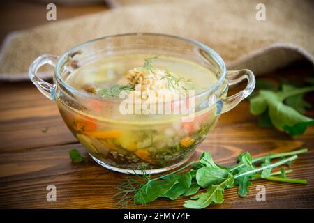 fresh hot soup with chicken meatballs and vegetables in a plate on a wooden table Stock Photo