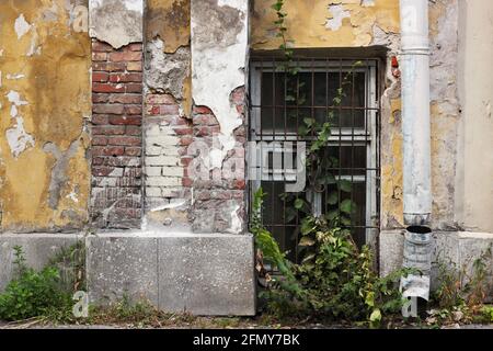 An old brick building with peeling off paint and a basement window with a lattice Stock Photo