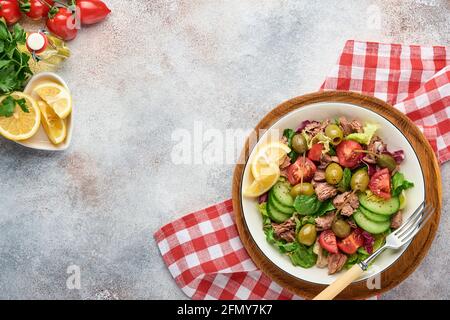 Tuna salad with fresh vegetables, olives, capers and lemon served in bowl on light grey background. Top view with copy space. Stock Photo