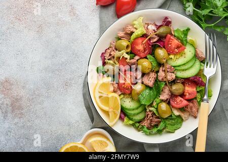 Tuna salad with fresh vegetables, olives, capers and lemon served in bowl on light grey background. Top view with copy space. Stock Photo