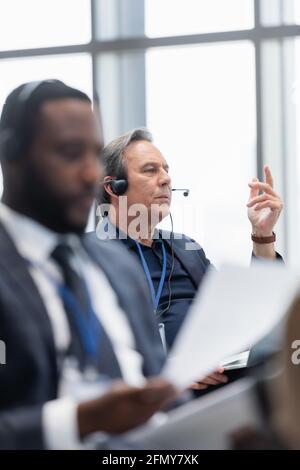 Mature businessman in headset holding laptop and talking during conference Stock Photo