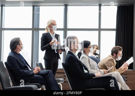 young businesswoman in medical mask holding notebook while asking question during seminar Stock Photo