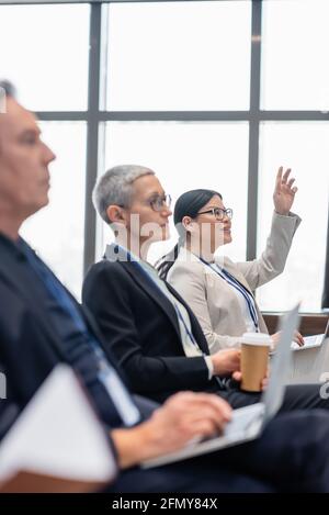 Smiling asian businesswoman raising hand near business people during conference Stock Photo