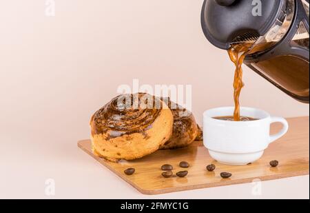 Pouring black coffee into a white cup. Two freshly baked cinnamon rolls. Copy space. Stock Photo