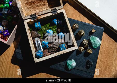 Image of a wooden box with blue role-playing game dice on top of a black notebook with green crystals and metal dice. Stock Photo